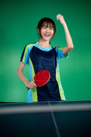 Photo for Female player holding paddle with fist up while winning a ping pong match - Royalty Free Image