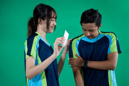 Photo for Male athlete in pain in arm muscles with female athlete holding a tube of medicine on a green screen background - Royalty Free Image