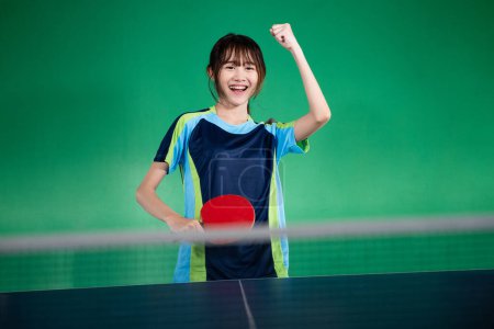 Photo for Asian female player holding bet with fist while winning ping pong match - Royalty Free Image