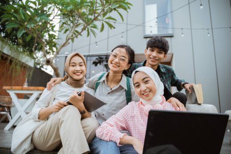 Photo for Smiling young people working together on a laptop sitting against a building in the background - Royalty Free Image