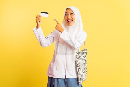 Téléchargez les photos : Veiled high school girl showing blank card with pointing finger on isolated background - en image libre de droit