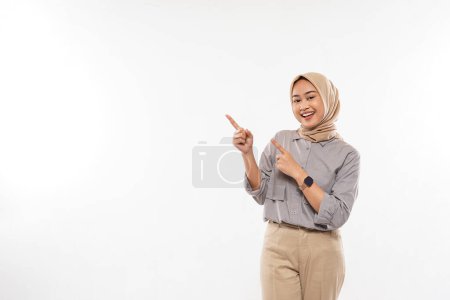 Téléchargez les photos : A young woman with hijab standing with smile and excitedly pointing on the empty space at her right side on the white background - en image libre de droit