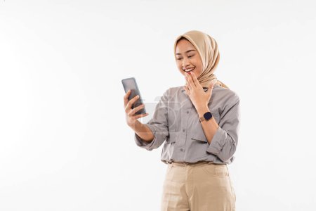 Téléchargez les photos : A young woman with hijab standing and put her hand in front of her mouth while looking at her phone - en image libre de droit