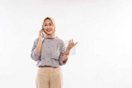 Téléchargez les photos : A beautiful woman with hijab standing and swing her hand while calling someone on phone on the white background - en image libre de droit
