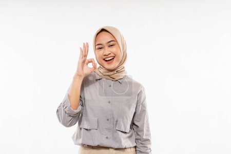 Téléchargez les photos : A beautiful woman with hijab standing facing forward with ok hand gesture and smiling with the white background and zoom in mode - en image libre de droit