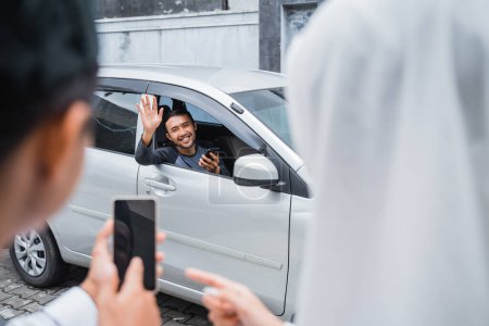 Foto de Conductor masculino en un coche olas como él cumple con los clientes que ordenan en línea - Imagen libre de derechos