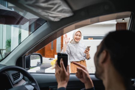 Foto de Asian veiled woman waves to online taxi driver when he comes to pick her up - Imagen libre de derechos