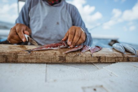 Foto de Fishermans hand cuts open a fish with a knife for fishing bait - Imagen libre de derechos