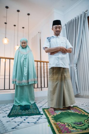 Téléchargez les photos : L'homme asiatique mène la prière avec la femme pendant le mouvement Sourate Al-Fatihah quand il prie sur un tapis de prière à la maison - en image libre de droit