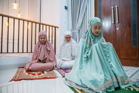 Téléchargez les photos : Three Asian Muslim women in Muslim clothing with hijabs praying in congregation in the prayer room - en image libre de droit