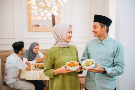 Téléchargez les photos : Portrait de mari et femme servant de la nourriture pour un ami et sa famille pour le petit déjeuner jeûnant ensemble pendant le ramadan - en image libre de droit