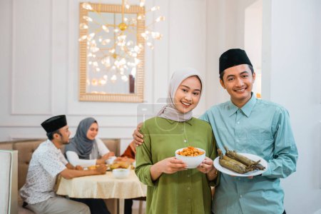 Téléchargez les photos : Portrait de mari et femme servant de la nourriture pour un ami et sa famille pour le petit déjeuner jeûnant ensemble pendant le ramadan - en image libre de droit