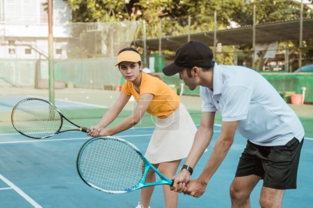 Téléchargez les photos : Entraîneur masculin donne un exemple d'une position de balle prête à recevoir pour une joueuse sur le court de tennis - en image libre de droit