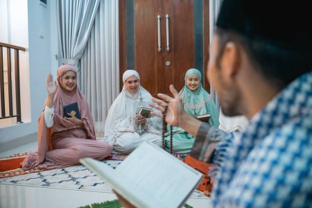 Photo for Female recitation participants raise their hands when asking questions to the recitation leader called kyai reciting the Quran at home - Royalty Free Image