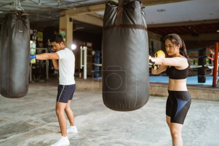 Téléchargez les photos : Le boxeur masculin et féminin frappant le sac de sable. entraîneur de boxe avec partenaire dans l'entraînement de gymnastique - en image libre de droit