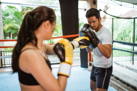 Téléchargez les photos : Un entraîneur de boxe masculin portant les coussinets pendant l'entraînement avec le boxeur féminin à l'intérieur de l'anneau de la boîte - en image libre de droit