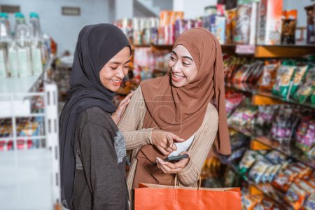 Téléchargez les photos : Deux belles filles musulmanes utilisant un smartphone tout en faisant du shopping ensemble au supermarché - en image libre de droit