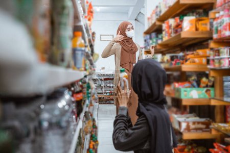 Téléchargez les photos : Fille musulmane dans le masque avec les pouces vers le haut signe d'approbation tout en faisant du shopping avec des amis en magasin - en image libre de droit