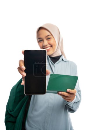 Photo for Portrait of smiling Asian Muslim woman showing blank phone screen and savings book on white background - Royalty Free Image