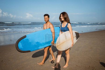 summer travel vacation happy couple friends walking along the beach carrying surfboards