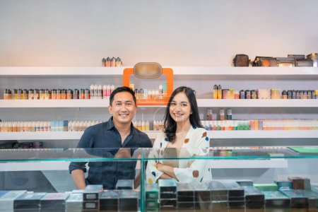 Photo for Couple of vape shopkeeper standing with smile behind the display table - Royalty Free Image