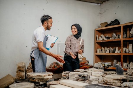 Camarero masculino sirviendo a una cliente musulmana bromeando mientras muestra productos de piedra en una tienda de artesanía de piedra