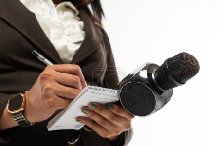 Photo for The hand of a journalist writing on a notebook using a black pen and bring a black microphone - Royalty Free Image