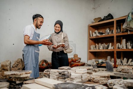 Foto de Asistente de tienda masculina sirve a una cliente musulmana mientras sostiene un arte de piedra en una tienda de artesanía de piedra - Imagen libre de derechos