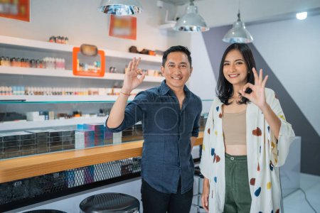 Photo for Couple of vape seller standing back to back with oke hand gesture inside the vape shop - Royalty Free Image