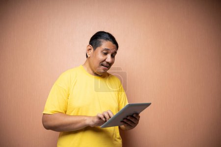 Photo for Old asian man holding tablet with left hand and showing typing gesture in plain background isolated - Royalty Free Image