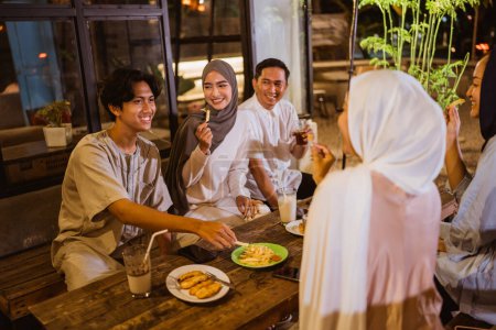 Téléchargez les photos : Jeunes musulmans asiatiques rompent rapidement ensemble en mangeant des collations d'abord dans un restaurant en plein air - en image libre de droit