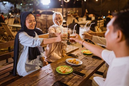 Téléchargez les photos : Tourné de deux femmes musulmanes voilées portant un toast en verre avec des amis avant de rompre le jeûne - en image libre de droit