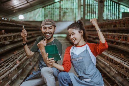 Téléchargez les photos : Heureux travailleurs masculins et féminins tenant un livre d'épargne les mains serrées dans une ferme de poulet - en image libre de droit