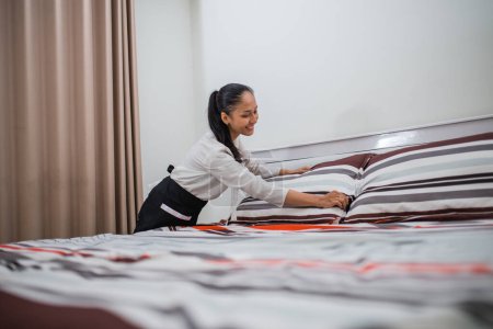 Photo for Asian woman maid fluffing pillows at work fluffing beds in hotel room - Royalty Free Image