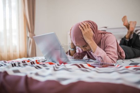 Photo for Muslim woman gets dizzy when using laptop while lying on the bed in the room - Royalty Free Image