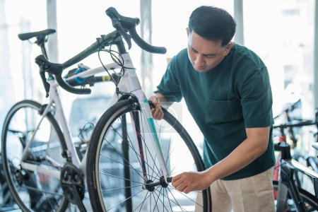 Téléchargez les photos : Employé masculin installe un pneu de vélo tout en travaillant à assembler des vélos dans un magasin de vélos - en image libre de droit