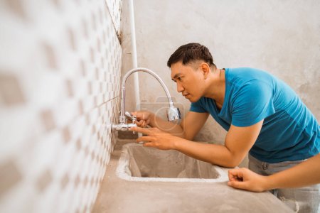 Téléchargez les photos : Asiatique jeune mari installe un robinet de lave-vaisselle tout en construisant une nouvelle maison - en image libre de droit