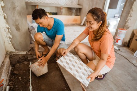 Frau bringt Fliesen, wenn Ehemann als Bauarbeiter beim Bau eines neuen Hauses Fliesen verlegt