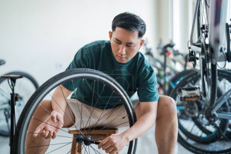 Téléchargez les photos : Jeune homme asiatique installe essieux tout en travaillant dans un magasin de vélo - en image libre de droit