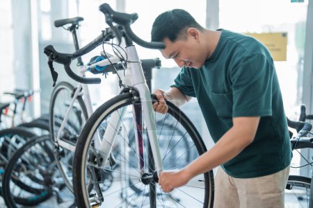 Téléchargez les photos : Jeune homme asiatique installe des pneus de vélo tout en travaillant sur l'assemblage de vélos dans un magasin de vélos - en image libre de droit