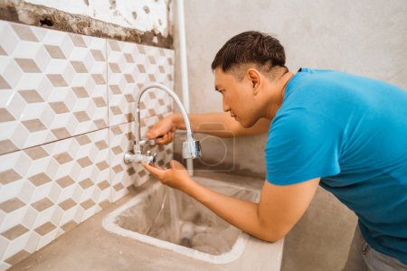 Téléchargez les photos : Asiatique jeune homme installe un robinet de lave-vaisselle tout en rénovant la maison - en image libre de droit