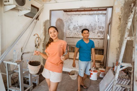Téléchargez les photos : Jeune couple portant des seaux et des pelles dans une maison en construction - en image libre de droit