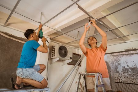 Téléchargez les photos : Jeune couple asiatique fixe plafond et installe des luminaires tout en rénovant une nouvelle maison - en image libre de droit