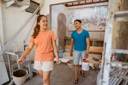 Téléchargez les photos : Jeune couple travaillant avec des seaux de ciment et des pelles sur une maison en construction - en image libre de droit