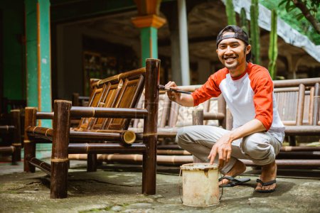 Téléchargez les photos : Un artisan utilisant des pinceaux et des laques lors de la finition de la chaise en bambou artisanat à l'extérieur de la maison - en image libre de droit