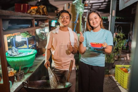 Téléchargez les photos : Mâle et femelle debout derrière le chariot de nourriture traditionnelle avec le pouce vers le haut geste - en image libre de droit