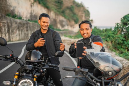 Téléchargez les photos : Cavalier indonésien assis sur la moto et tenant téléphone écran de maquette - en image libre de droit