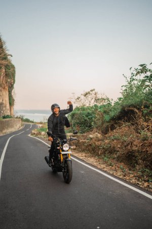 Téléchargez les photos : Cavalier indonésien debout en moto avec geste de pompe poing - en image libre de droit