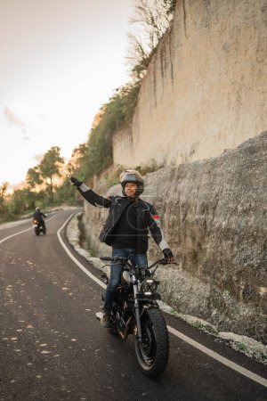Téléchargez les photos : Asiatique homme debout tandis que équitation moto avec ouvert bras geste - en image libre de droit