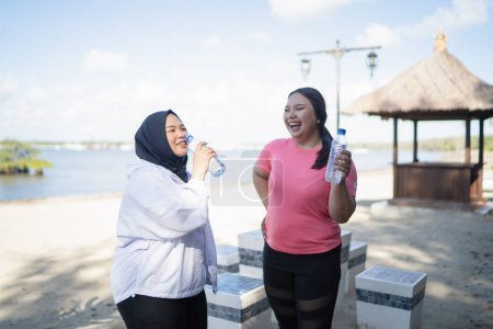Téléchargez les photos : Femmes asiatiques debout et boire de l'eau minérale en plein air - en image libre de droit